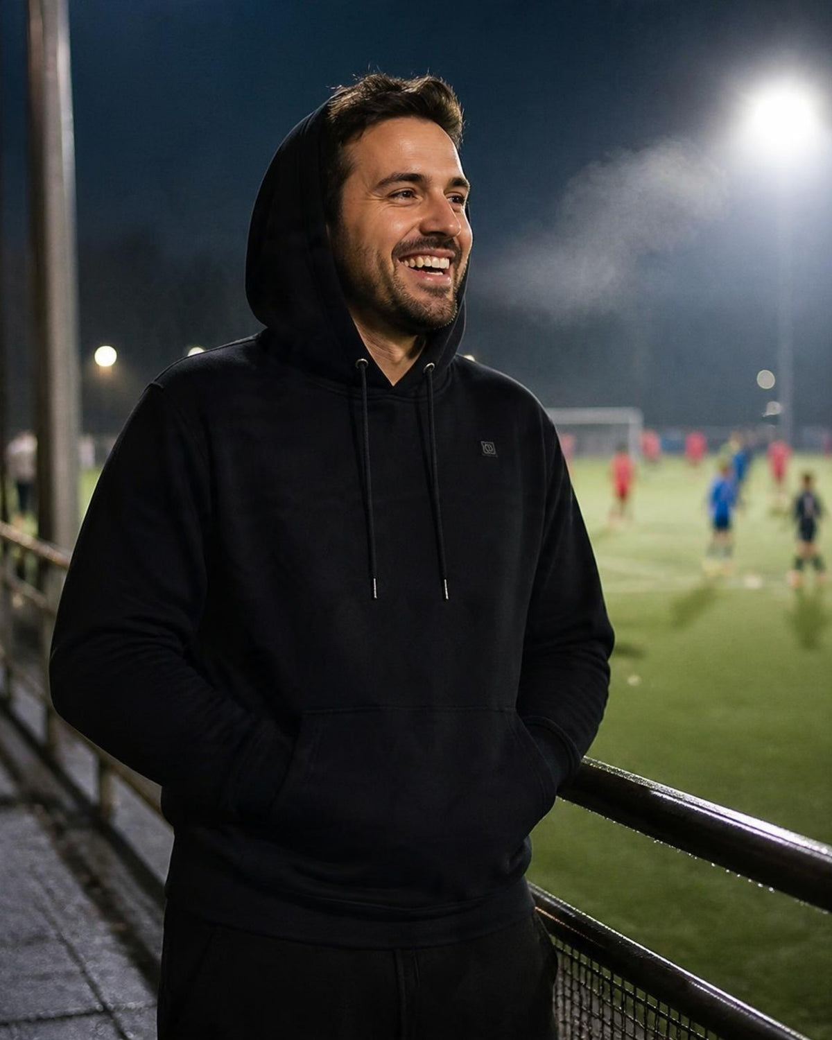 Mann im schwarzen ArticLux Wärmenden Hoodie abends am Fußballplatz