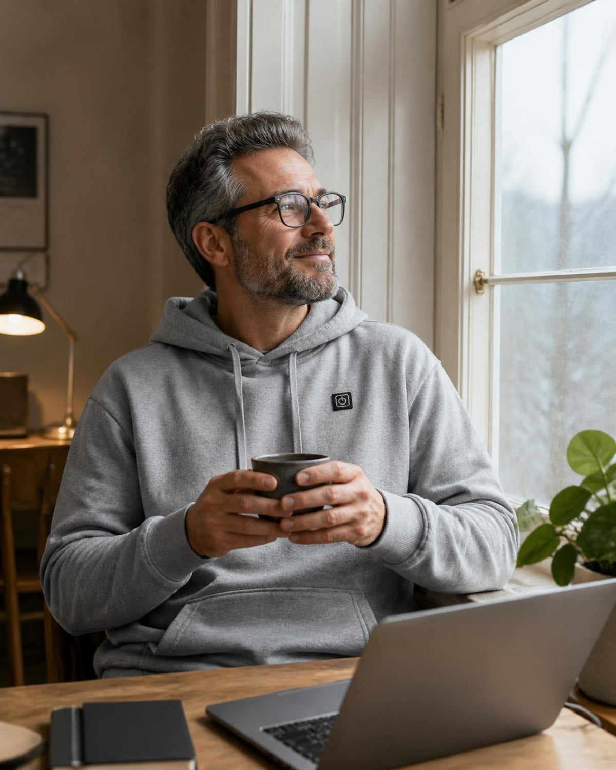 Mann im grauen ArticLux Wärmenden Hoodie im Homeoffice mit Tee