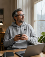 Mann im grauen ArticLux Wärmenden Hoodie im Homeoffice mit Tee
