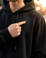 Finger drückt die Bedientaste an der Brust des schwarzen ArticLux Wärmenden Hoodies