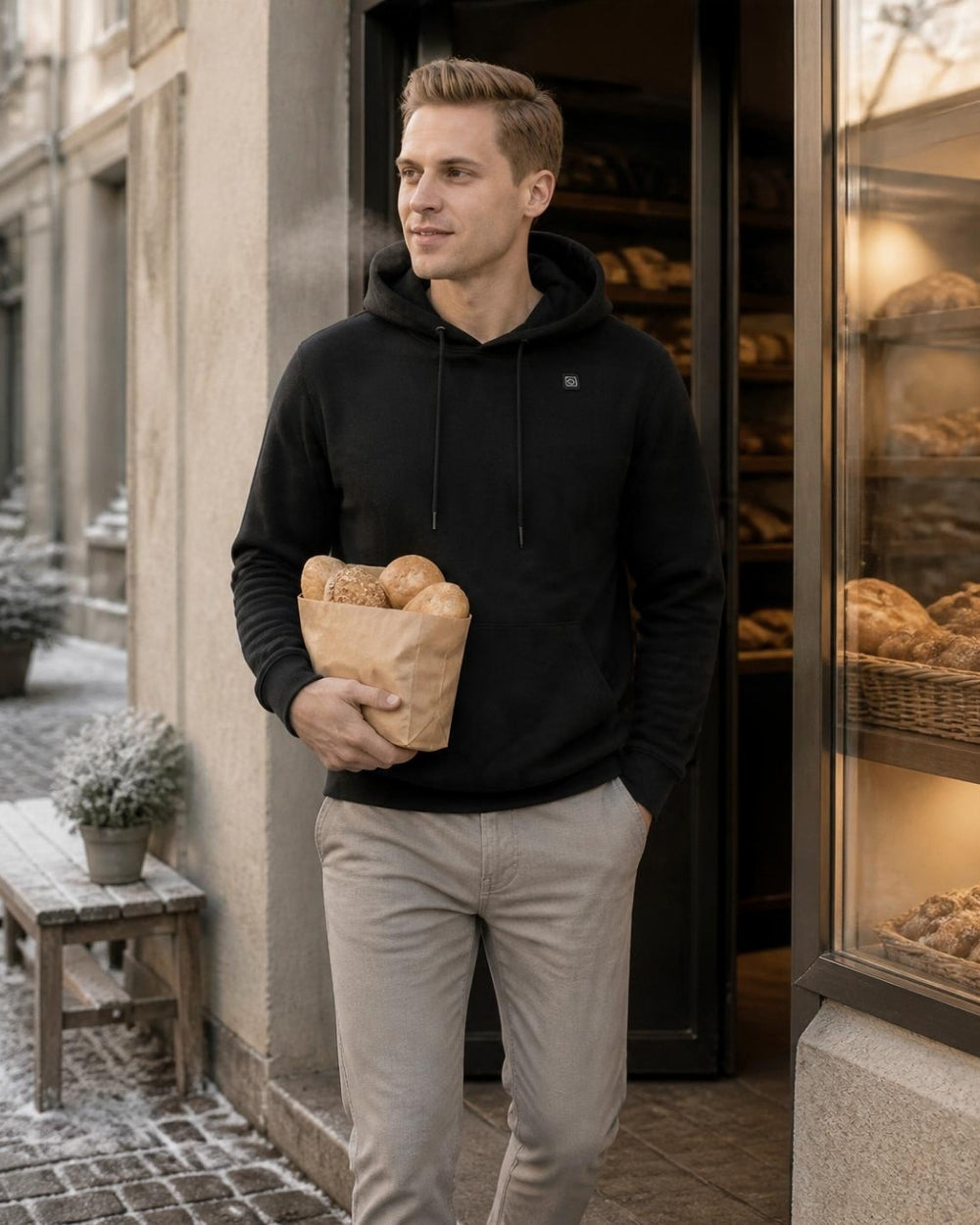 Mann im schwarzen ArticLux Hoodie mit Brötchentüte vor einer Bäckerei