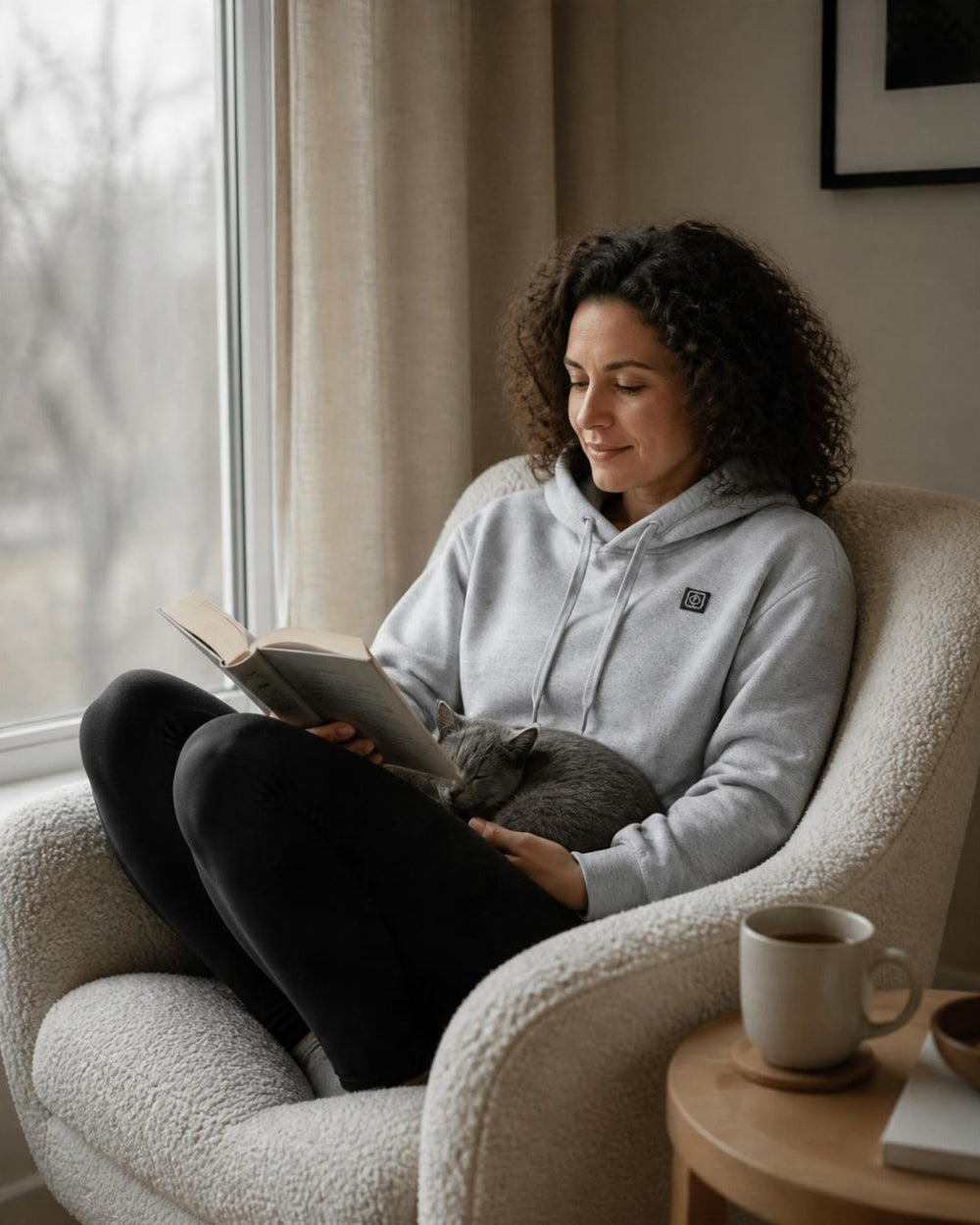 Frau im grauen ArticLux Hoodie liest im Sessel am Fenster